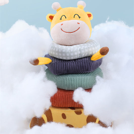 Stack of colorful sweaters with a plush giraffe toy on top against a light blue background