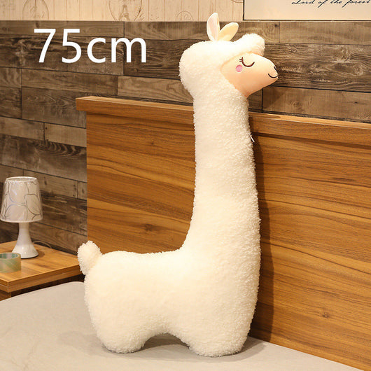 White plush llama toy next to a wooden shelf with a lamp and small plant.