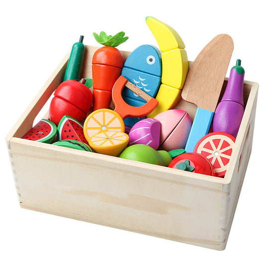 Colorful wooden toy set of fruits, vegetables, and kitchen utensils in a wooden box on a white background.