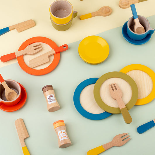 Colorful children's play kitchen set with plates, cups, and utensils on a light green background.