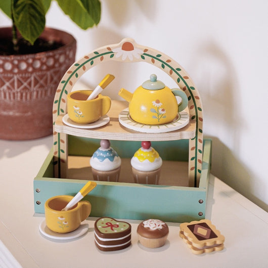 Toy tea set with a wooden stand on a light surface, featuring a teapot, cups, and cookies.