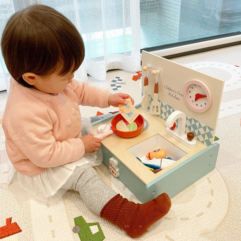 Child playing with a toy kitchen set on a carpeted floor.