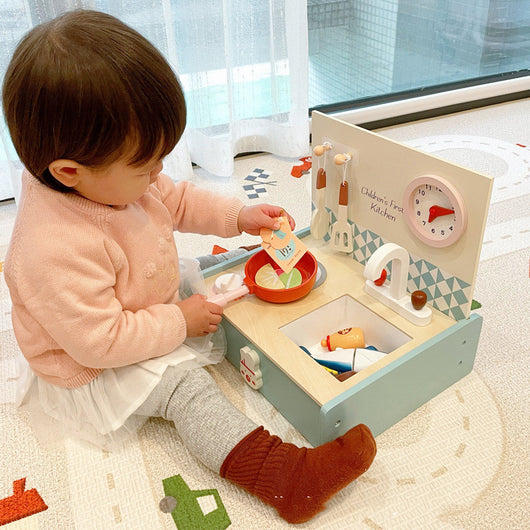 Child playing with a toy kitchen set on a carpeted floor.