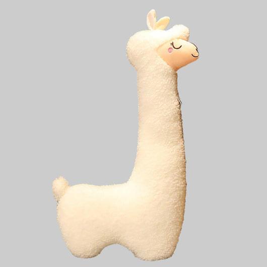 Plush llama toy against a wooden wall with a lamp in the background