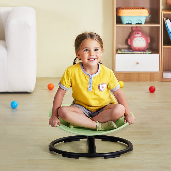 Child sitting on a green balance chair in a room with toys scattered around.