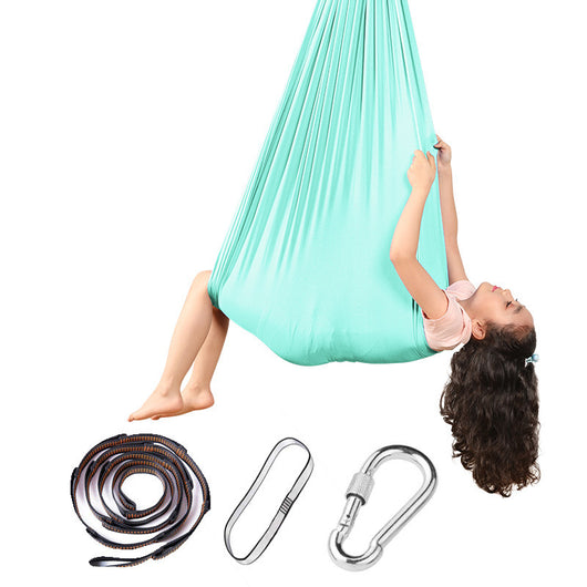 Child in a green aerial yoga hammock with accessories on a white background