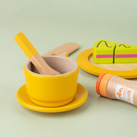 Yellow toy bowl with wooden spoon and salt container on a light green background