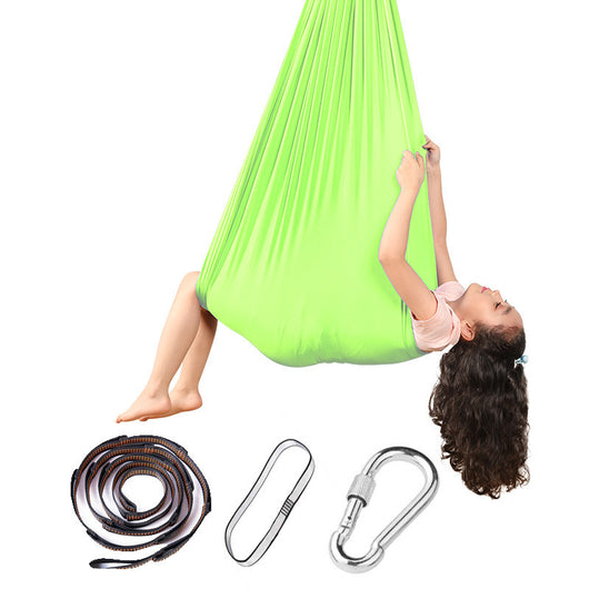 Child in a green aerial yoga hammock with accessories on a white background