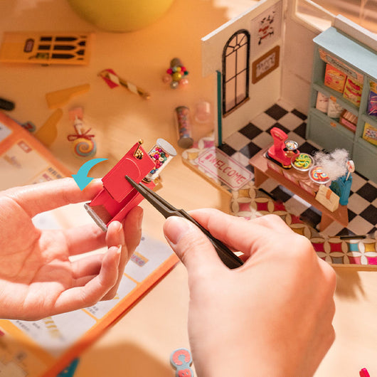 Person assembling a small model of a building with miniature furniture and decor.