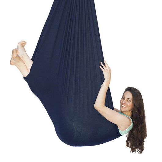 Woman in a navy blue aerial yoga hammock on a white background