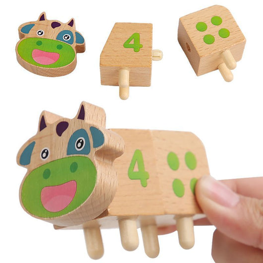 Wooden cow toy with number 4 and green feet, held by a hand on a white background